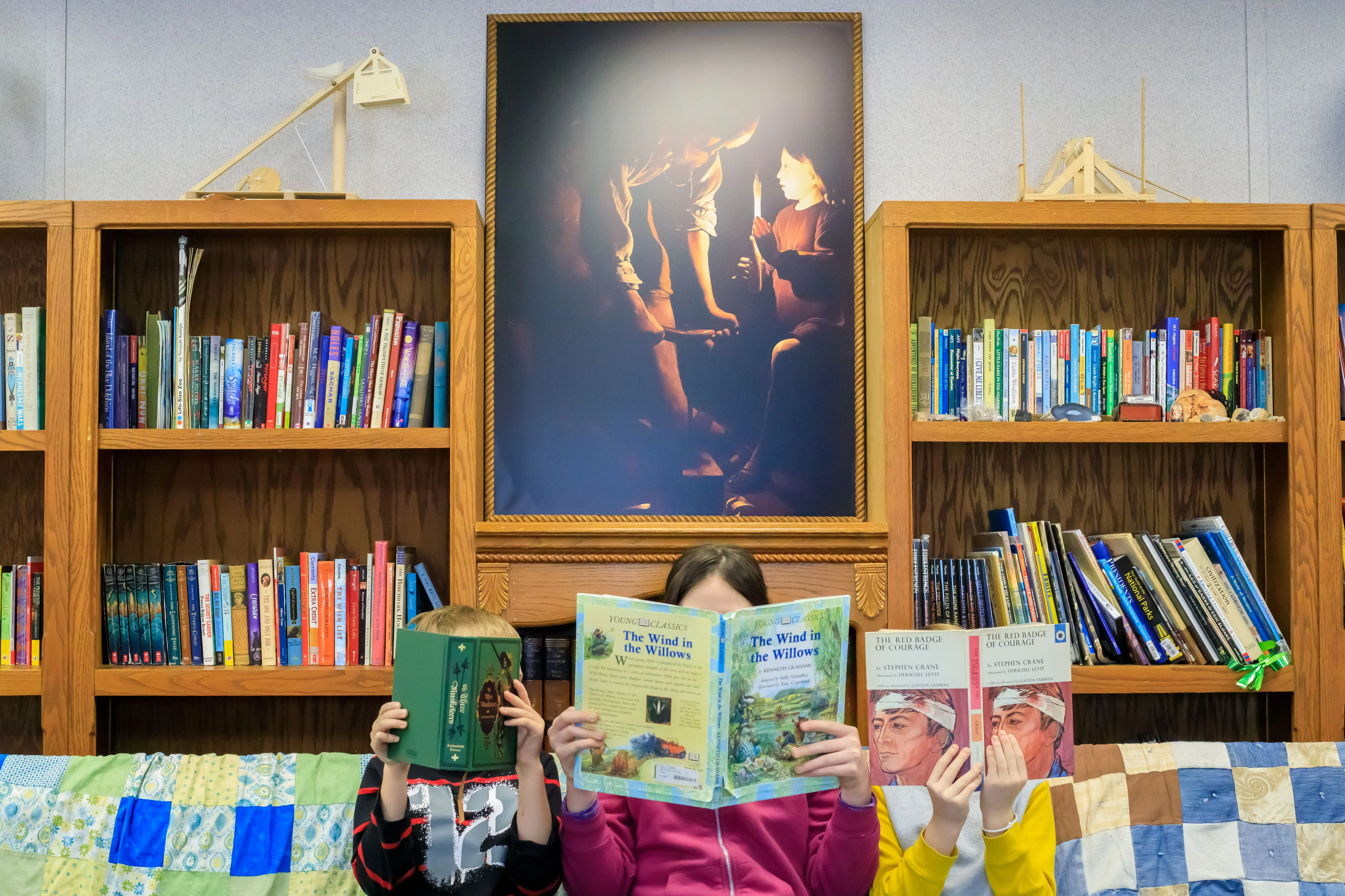 Three students read in the library with artwork behind them