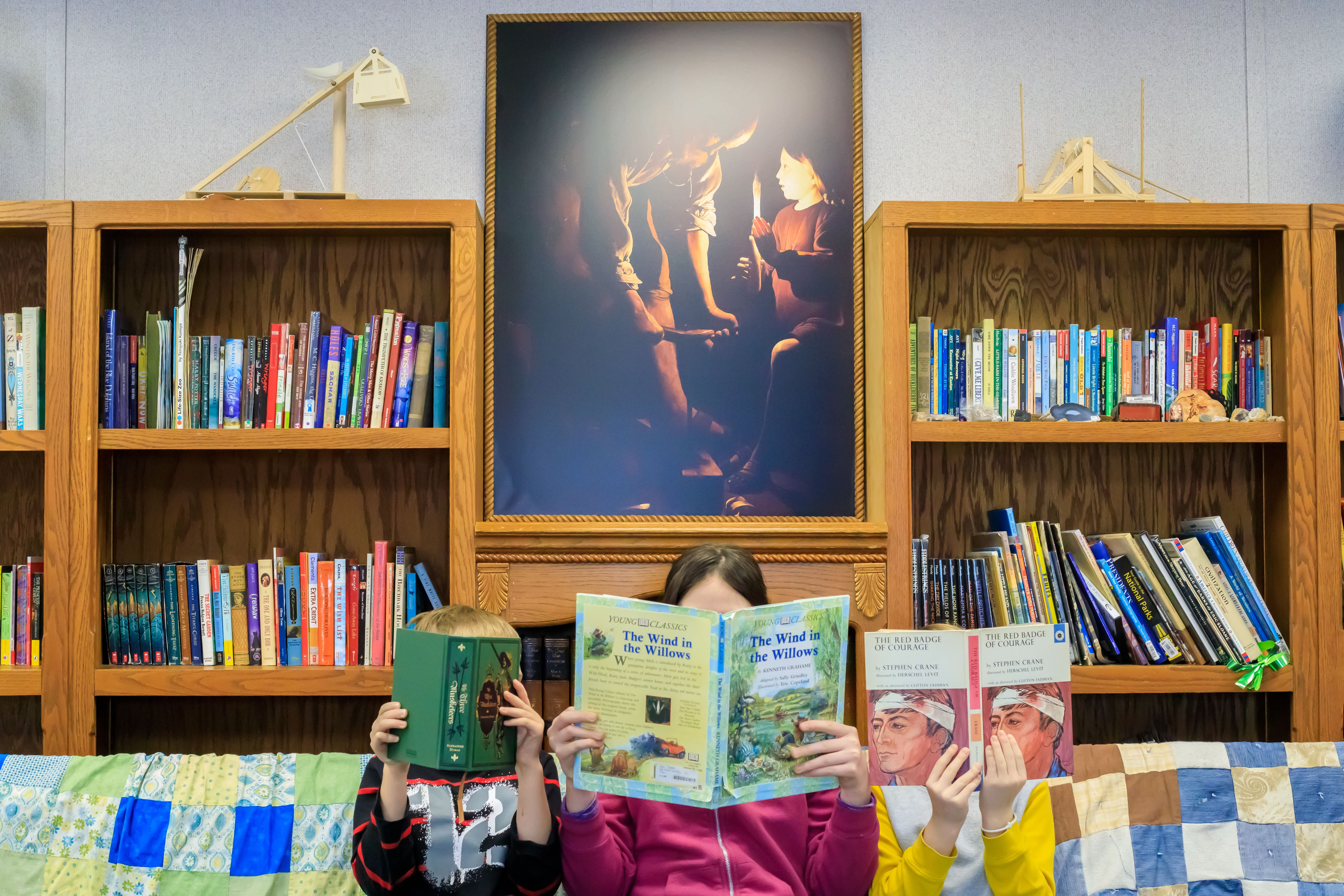 Three students read in the library with artwork behind them
